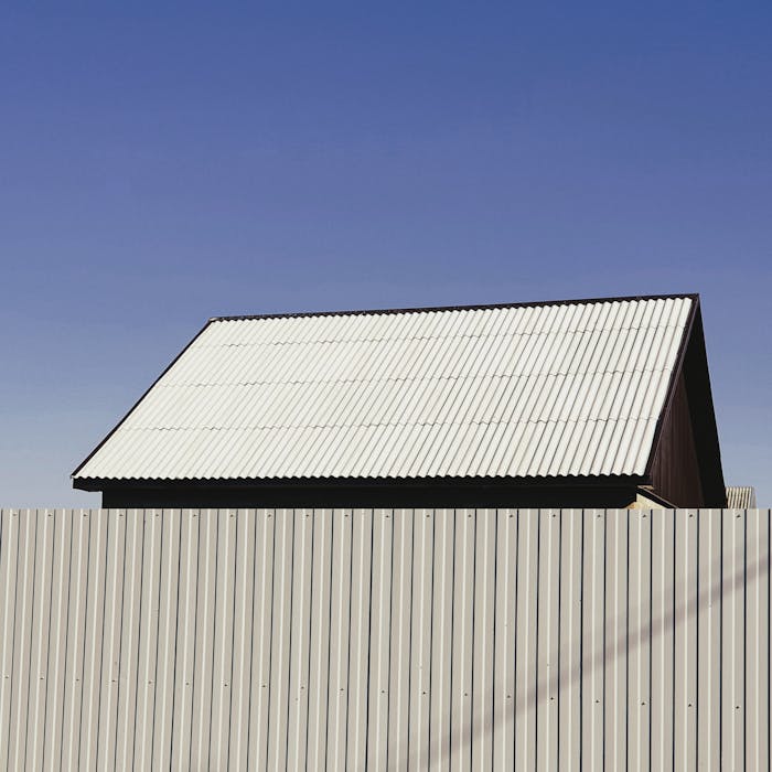 A simple structure with a metal roof and fence under a clear blue sky, showcasing minimalist architecture.